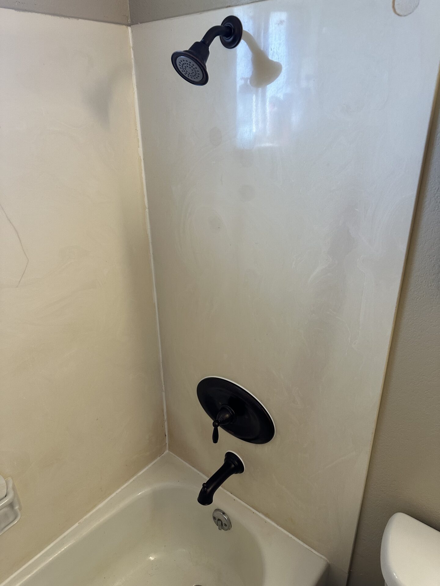 A bathtub and shower with a black showerhead, faucet, and handle, set against a plain, light-colored wall.