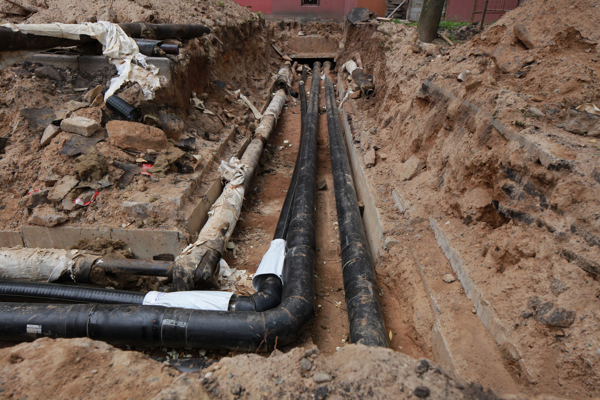 Underground utility pipes laid in a trench with exposed soil and construction materials visible around the site.